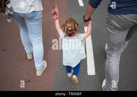 Coppia sposata camminando mano nella mano con il loro primo figlio aiutandola ad equilibrio come ella è imparare a camminare Foto Stock