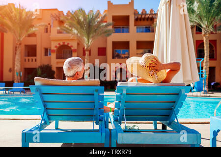Coppia senior a rilassarci in piscina giacente sulla chaise-longue. Le persone che si godono le vacanze estive. Foto Stock