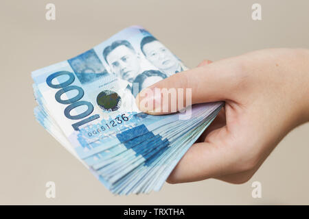 Mano che tiene ripiegato di blu denaro in contanti di mille Filippine pesos. Dando corrompere, pagare le bollette o ottenere lo stipendio. Pagamento il giorno! Foto Stock