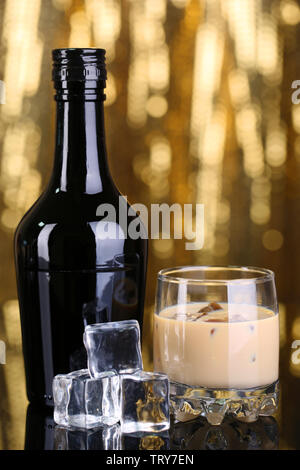 Il Baileys liquore in bottiglia e vetro su sfondo dorato Foto Stock