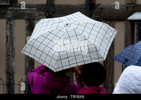 Turisti stranieri con un ombrello a Stratford-upon-Avon, Warwickshire, Regno Unito Foto Stock