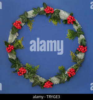 Inverno e ghirlanda di Natale con holly, coperta di neve abete rosso, ivy e cedro su sfondo blu con una copia dello spazio. Simbolo tradizionale per la festosa Foto Stock