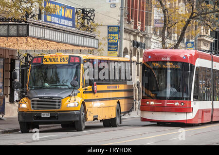 TORONTO, Canada - 14 novembre 2018: Toronto il tram che passa accanto a un giallo American School bus, del centro cittadino di Toronto, Ontario. Si tratta di uno dei simboli o Foto Stock