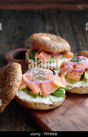 Lox - Tutto bagel con salmone affumicato, gli spinaci, le cipolle rosse, avocado e crema di formaggio su una tavola in legno rustico sfondo. Messa a fuoco selettiva. Foto Stock