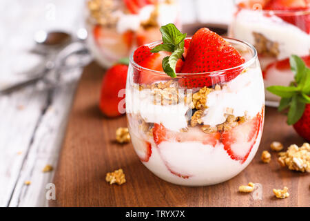 Sana colazione di fragola parfaits fatta con frutta fresca, yogurt e granola su un rustico tavolo bianco. Messa a fuoco selettiva. Foto Stock