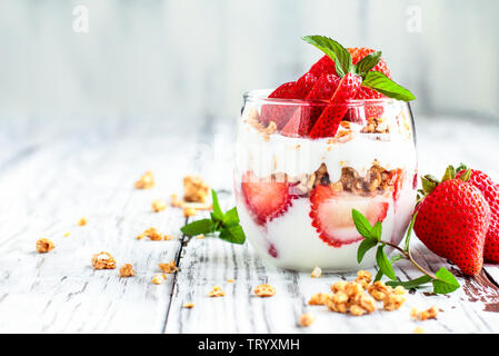 Sana colazione di fragola parfaits fatta con frutta fresca, yogurt e granola su un rustico tavolo bianco. Messa a fuoco selettiva. Foto Stock