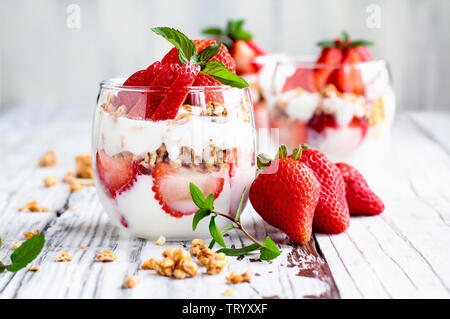 Sana colazione di fragola parfaits fatta con frutta fresca, yogurt e granola su un rustico tavolo bianco. Messa a fuoco selettiva. Foto Stock