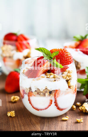 Sana colazione di fragola parfaits fatta con frutta fresca, yogurt e granola sopra una tavola in legno rustico. Messa a fuoco selettiva. Foto Stock