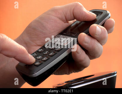 Mano d'uomo tenendo un vivavoce del telefono di rete fissa premendo un numero sul tastierino per effettuare una chiamata. Foto Stock