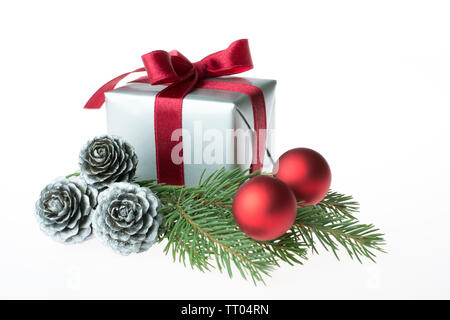 Composizione di natale con un regalo avvolto con nastro rosso, argento coni, baubles rosso e un abete branch - close-up isolati su sfondo bianco Foto Stock