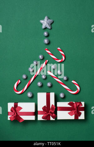 Albero di natale concetto con confezioni regalo, candy canes, globuli di glitter e silver star su sfondo verde Foto Stock