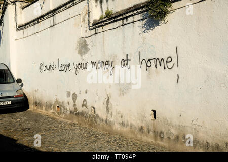 Graffiti su un muro bianco volto a turisti nel quartiere Albaicin di Granada, Spagna: '@turistiche: lasciare i vostri soldi a casa!" Foto Stock