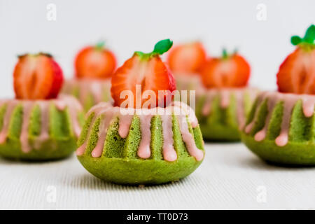 Verde Matcha tè Mini Bundt torte spruzzata con smalto di fragola e guarnita con fragole fresche tagliate a metà Foto Stock