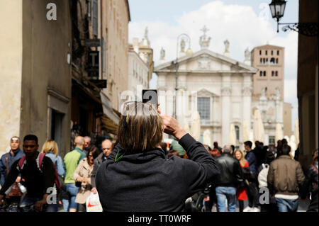 Primo piano del turista uomo sulla strada a Mantova, prendendo foto di Piazza Sordello con il telefono. Mantova, Italia Foto Stock
