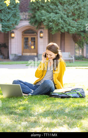 Felice, sorridente, giovane donna collegio femminile studente universitario con computer portatile parlando al cellulare all'esterno del campus Foto Stock