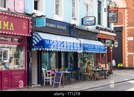 Una coppia matura seduti a un tavolo sul marciapiede esterno Maison Bertaux, a19th-secolo pasticceria francese e sale da tè in Greco Street, Soho, Londra Foto Stock