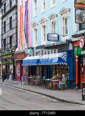 Una coppia matura seduti a un tavolo sul marciapiede esterno Maison Bertaux, a19th-secolo pasticceria francese e sale da tè in Greco Street, Soho, Londra Foto Stock