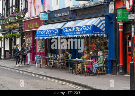 Una coppia matura seduti a un tavolo sul marciapiede esterno Maison Bertaux, a19th-secolo pasticceria francese e sale da tè in Greco Street, Soho, Londra Foto Stock