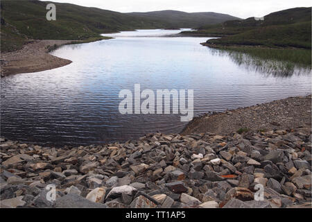 Una vista sul Loch un Chroisg in Scozia vicino a Ullapool con impilate le rocce per formare una barriera in primo piano e le colline circostanti Foto Stock