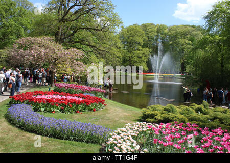 Vista in giardini Keukenhof guardando una fontana nel lago con i visitatori a piedi sul percorso e sulla giant pietre miliari vicino al bordo del lago. Foto Stock