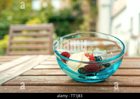 Gelato alla crema con frutti di bosco freschi su un blu vaschetta trasparente su un tavolo in legno all'esterno. Foto Stock