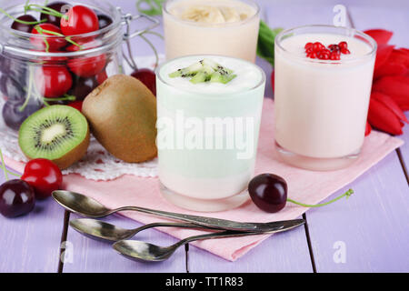 Delizioso yogurt con frutta gusti in bicchieri e frutta fresca sul colore di sfondo in legno Foto Stock