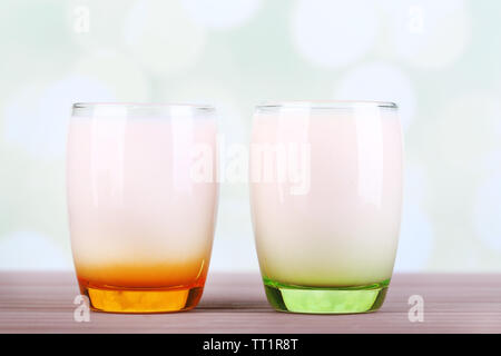 Delizioso yogurt con frutta gusti in bicchieri di colore sul tavolo di legno, su sfondo chiaro Foto Stock