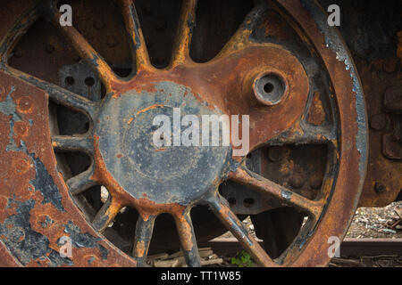 Close-up di vecchi circolare a raggi arrugginendo metallo colato stazione treno a vapore il motore ruota pronto per lavori di ristrutturazione a Didcot Railway Centre, Oxfordshire, Regno Unito. Foto Stock