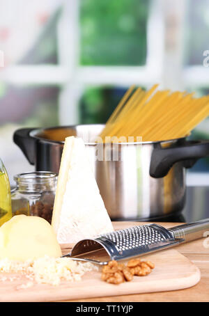 Processo di preparazione della pasta. Composizione con fila spaghetti in padella, grattugia, formaggio, sul tavolo di legno su sfondo lucido Foto Stock