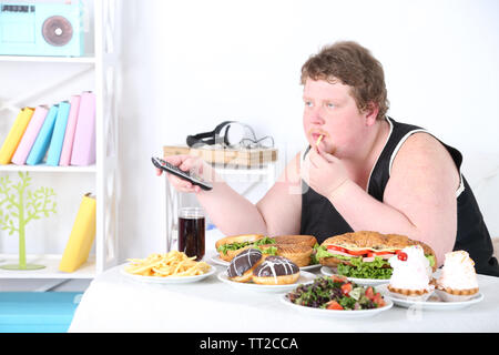 Uomo grasso ha un grande pranzo e guardare la TV in home page sul fondo interna Foto Stock