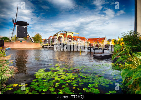 Basso Angolo di visione di un canale con un piccolo ponte e il mulino a vento, Leiden, Olanda meridionale, Paesi Bassi Foto Stock