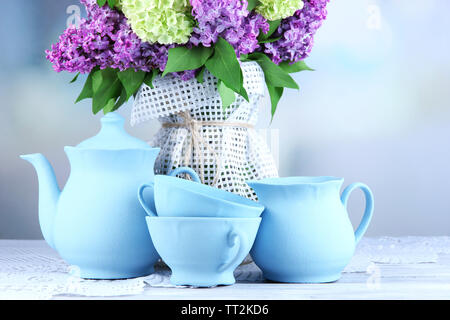 Composizione con set per il tè e bellissimi fiori primaverili in vaso, sul tavolo di legno, su sfondo lucido Foto Stock