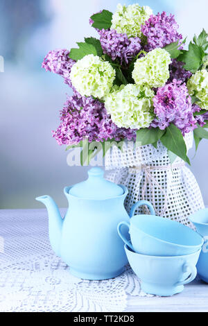 Composizione con set per il tè e bellissimi fiori primaverili in vaso, sul tavolo di legno, su sfondo lucido Foto Stock