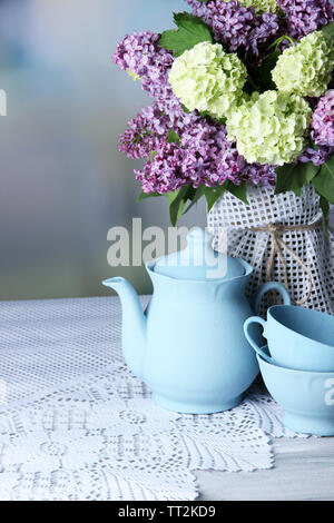 Composizione con set per il tè e bellissimi fiori primaverili in vaso, sul tavolo di legno, su sfondo lucido Foto Stock