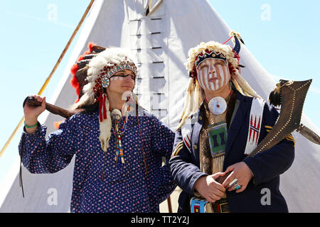 Indiani del Nord America stand con arma vicino a wigwam contro il cielo blu. La ricostruzione di native american life su Mosca festival storici Foto Stock