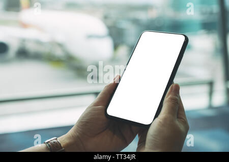 Mockup immagine di una donna di mani e utilizzando il nero telefono cellulare con schermo vuoto mentre è seduto in aeroporto Foto Stock