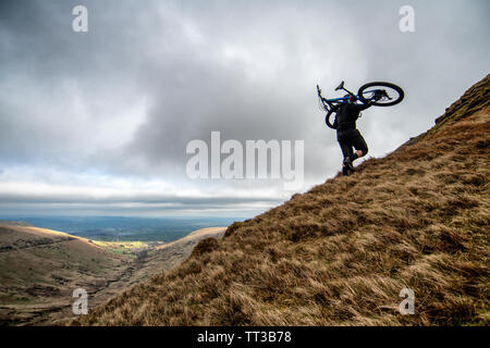 Un uomo che porta una mountain bike sulle sue spalle al vertice dei fan-y-grande nel Parco Nazionale di Brecon Beacons, Galles. Foto Stock