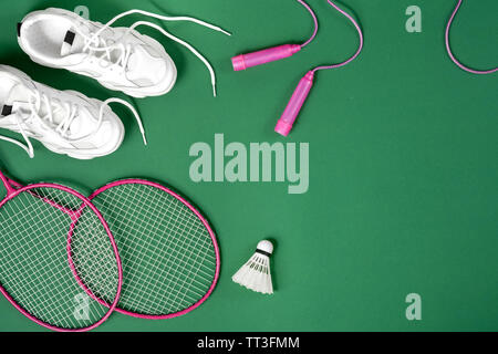 Attrezzature sportive. Volano e badminton racchetta, corda, sneakers su sfondo verde. Fitness, sport e stile di vita sano concetto. Foto Stock