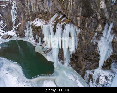 Foto aeree. Grandi ghiaccioli appesi da una scogliera congelati di un ruscello di montagna. Foto Stock