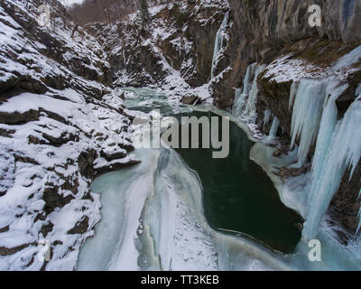 Grandi ghiaccioli appesi da una scogliera congelati di un ruscello di montagna. Foto Stock