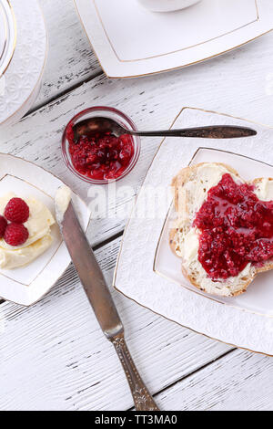 Toast freschi fatti in casa con burro e marmellata di lamponi sulla piastra su sfondo di legno Foto Stock