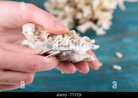 Mano con pinzette perla di contenimento e Ostrica su sfondo di legno Foto Stock