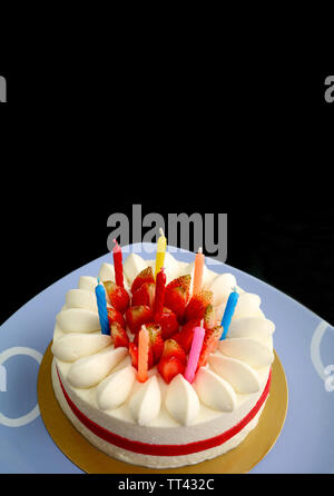 L'immagine verticale di fragola vaniglia breve torta con multi-colore candele preparando per la celebrazione su sfondo nero Foto Stock