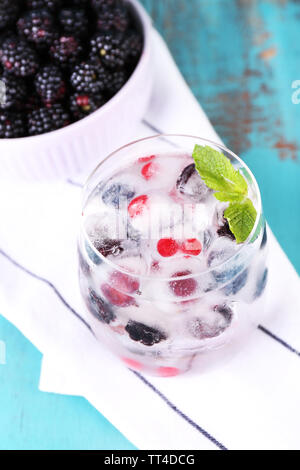 Cocktail a freddo con frutti di bosco, congelati in cubetti di ghiaccio e fresche blackberry nella ciotola sul colore di sfondo in legno Foto Stock
