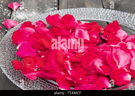 Petali di rosa giacciono su una piastra sul vecchio dark di tavole di legno. spa Foto Stock