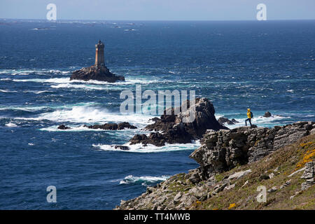 Donna in giacca gialla in piedi sul terreno roccioso a Pointe du Raz, uno di Bretagna le più drammatiche, punti di riferimento e il faro La Vieille, Franc Foto Stock