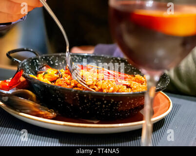 Mangiare paella valenciana in una padella nera con una forchetta. Piatti tipici della cucina spagnola. Frutti di mare e il turismo Foto Stock