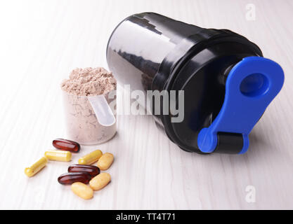 La proteina del siero di latte in polvere in scoop con vitamine e agitatore in plastica su sfondo di legno Foto Stock