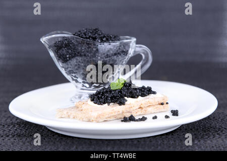 Fetta di pane con burro e sauceboat con caviale sulla piastra sul tessuto scuro dello sfondo Foto Stock