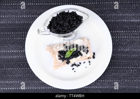 Fetta di pane con burro e sauceboat con caviale sulla piastra sul tessuto scuro dello sfondo Foto Stock